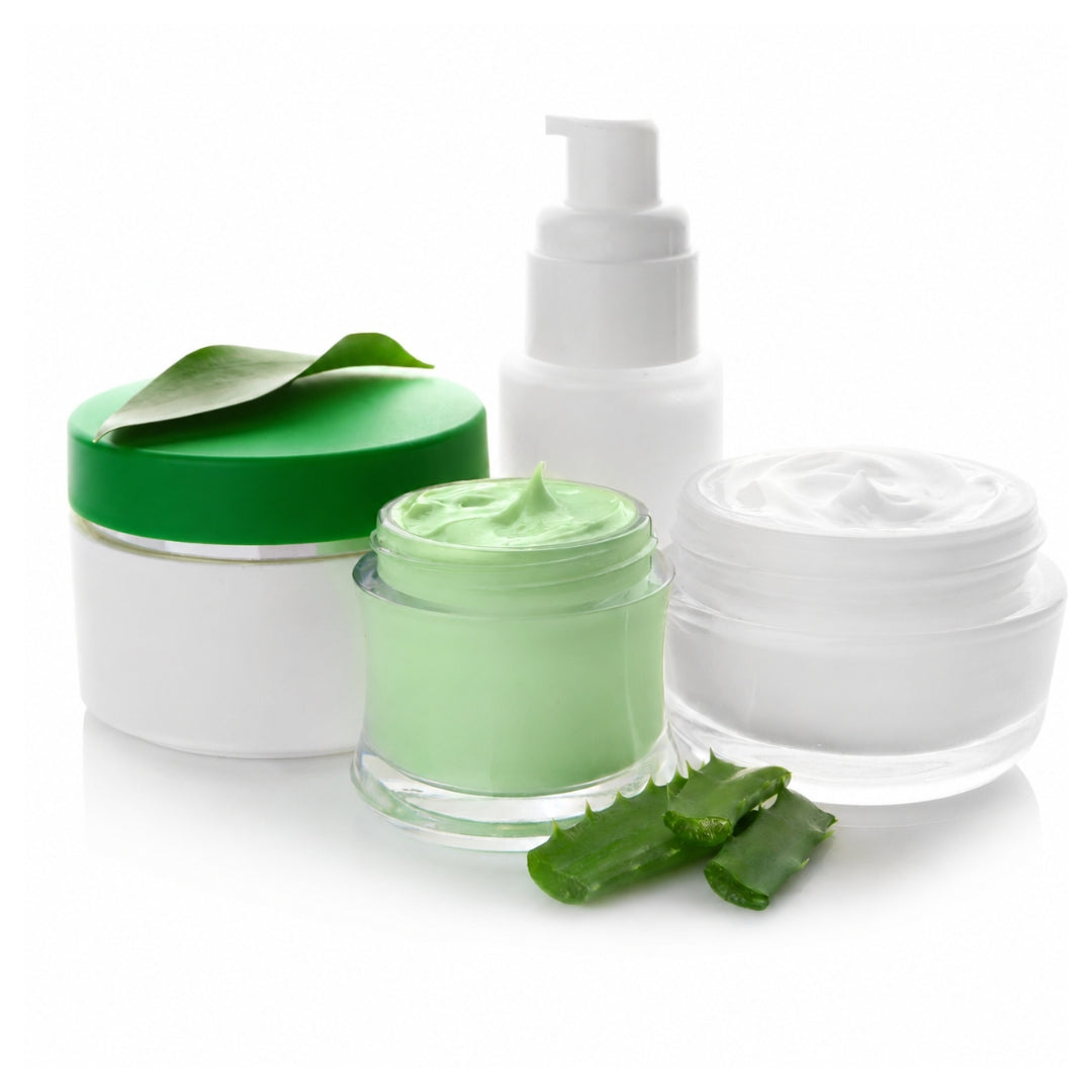 Three skincare containers on a white background: a white jar with a green lid and leaf decoration, a clear jar filled with pale green cream, and a white pump bottle. A small aloe vera slice rests in front.