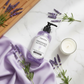 Lavender shower gel bottle surrounded by fresh lavender sprigs and spa accessories on white marble